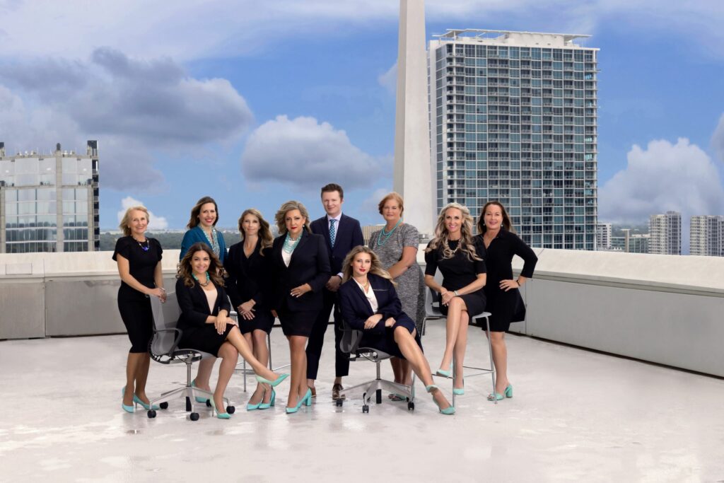 A group of women and one man dressed in business formal attire and posing on top of an office building.
